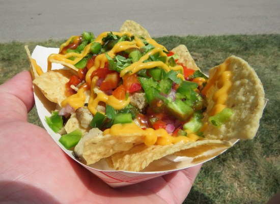 Nachos with several diced toppings, including peppers and a little bit of chicken. A modicum of nacho cheese is drizzled on.
