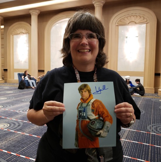 Anne holding an autographed 8x10 of Luke Skywalker in X-Wing pilot uniform.