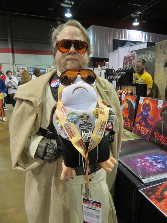 cosplay: Luke Skywalker from "The Last Jedi" carrying a Porg doll. Both are wearing brownish-orange sunglasses.