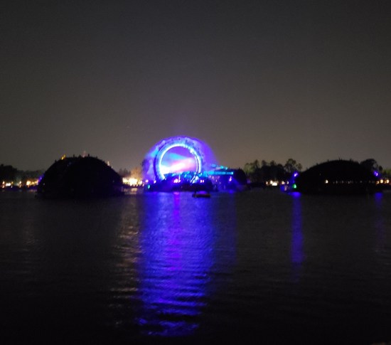 Distant nighttime Stargate across a lagoon with lightshow being fired up in its center. The evening sky is nearly white from Disney World light pollution.