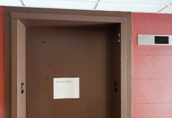 Elevator with piece of paper and simplistic printing: "Out of order. Sorry for the inconvenience. Staff."