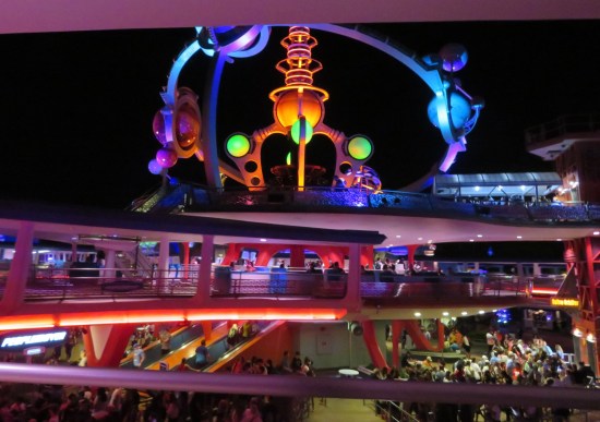 Slow, level, non-zooming roller coaster snakes around the park at night, lots of lights and Jetsons architecture.