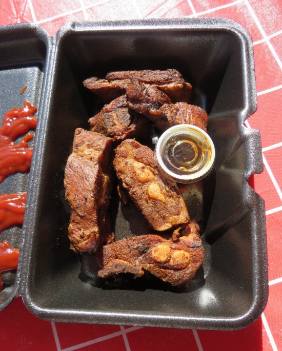 Six finger-sized sections of pork ribs served in the same container with one very tiny cup of sauce.