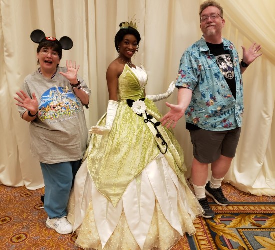 A Princess Tiana cast member in a yellow ballroom dress and tiara poses regally while Anne and I do jazz hands on either side of her.