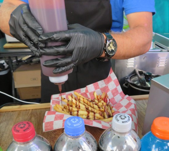 Guy with black gloves pouring chocolate on fries.
