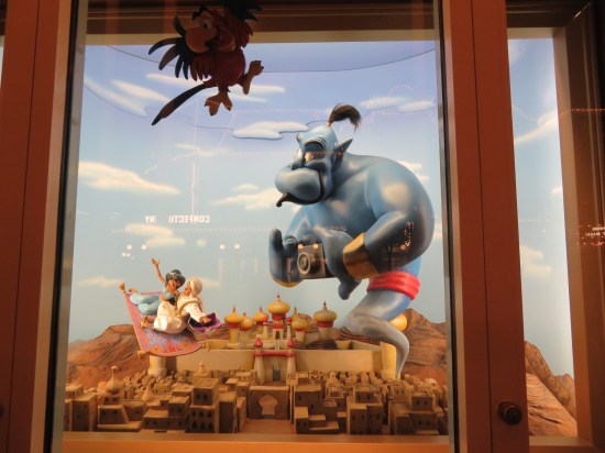 Window display of Prince Ali and Jasmine on the magic carpet over Agrabah. The Genie flies behind, holding a 35mm camera. Iago flies at the top for no story reason.