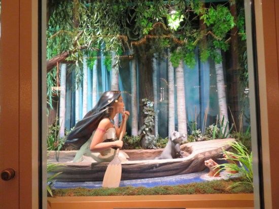 Window display of Pocahontas rowing a canoe down a forest creek. Meeko the raccoon sits in the front seat.