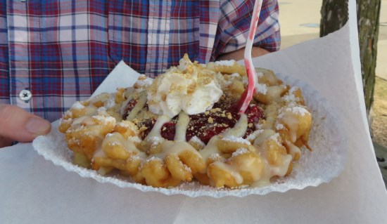 funnel cake topped with strawberries, glaze, cheesecake sauce and a dollop of whipped cream.