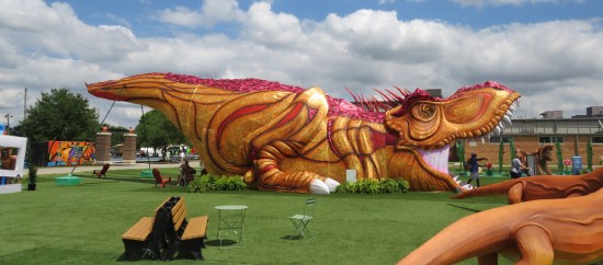 Side view of a T-Rex lying down with its mouth open and its tail sticking straight out horizontally.