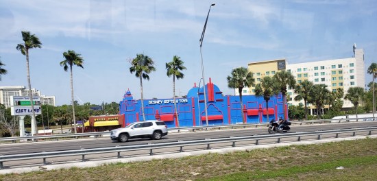 Shop with signs reading "Disney Gifts and Toys" and "Gift Land" along a Florida interstate; lots of palm trees.