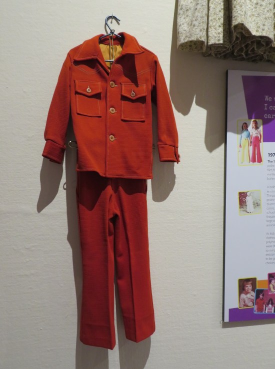Red jacket with yellow lining and creased red pants hanging on a white wall.