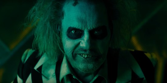 Shadowy Beetlejuice's face mugs directly into the camera, bathed in bluish-green light.