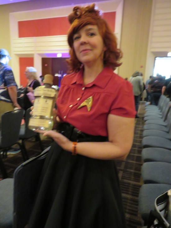 Lucy Ricardo cosplayer with a red shirt, Trek Delta pin, red hair bow, and a liquor bottle.