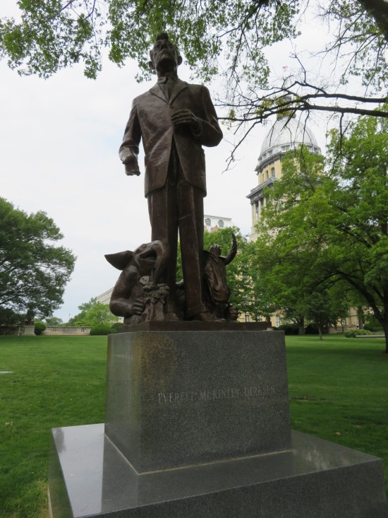 Statue of Everett Dirksen. One hand clasps a jacket button. At his feet are a tiny cartoon elephant and bull.