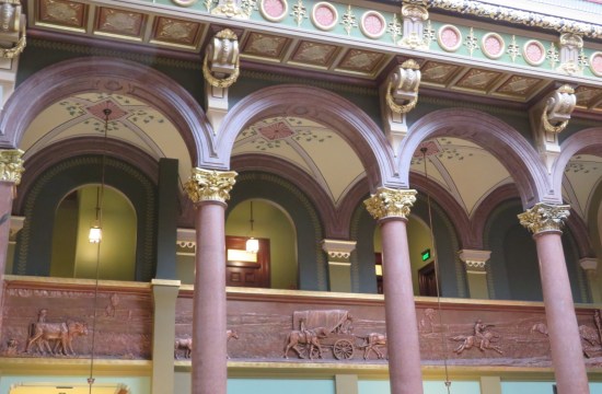 Upper floor with vaulted columns, arches, and a half-wall bearing a brown frieze of 19th-century pioneers and/or cowboys.