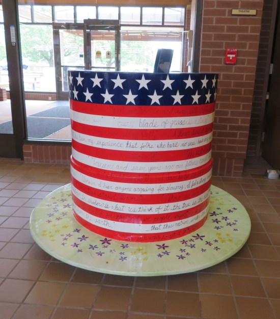 5-foot-tall top hat adorned with red and white stripes. The top row is blue with white stars. Quotes are written in each row in cursive.