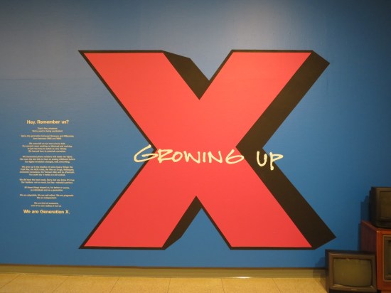 Blue wall with the exhibit title "Growing Up" written in white across a large red X.