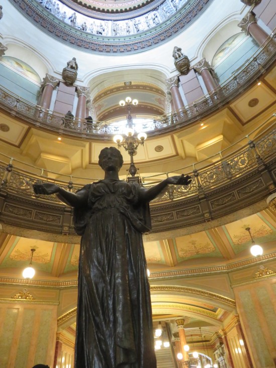 Bronze statue of a robed woman holding out her arms, elbows bent.