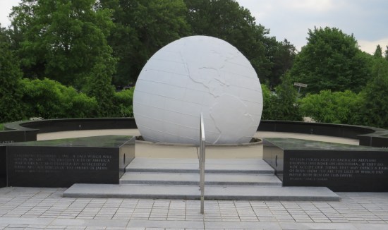 Large all-white globe on a concrete pedestal. Around it is a walkway surrounded by short, curved, black marble walls.