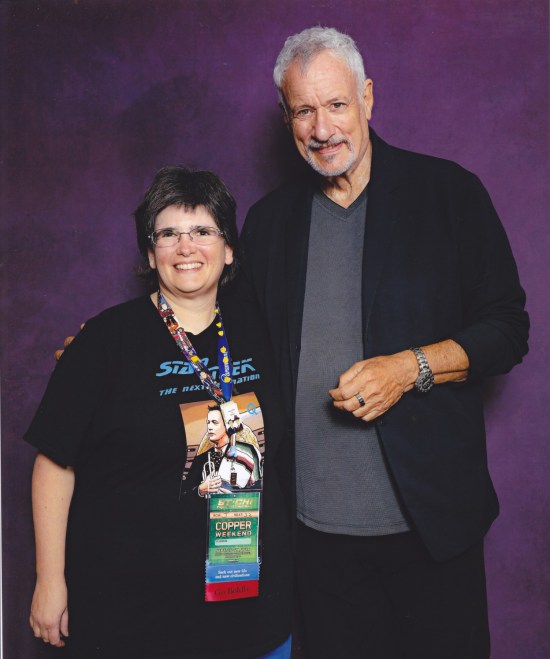 Anne with John de Lancie in front of a purple photo backdrop.