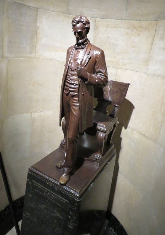 Statue of Lincoln standing with his head bowed and one hand holding his jacket lapel.