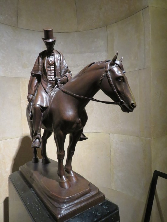 Statue of young-adult Lincoln on a horse, wearing a top hat and holding the reins. His face is weirdly shadowed.