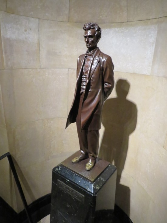 Statue of Lincoln with no beard and his hands clasped behind his back.