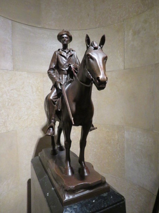 Statue of young Lincoln on a horse, holding a rifle and wearing a hat.