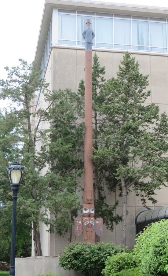 Two-story-tall totem pole with Native motifs at the base and Abraham Lincoln on top with both hands against his waist.