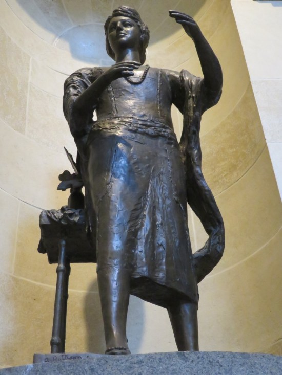 Statue of a woman in a modest dress and necklace, a boa draped on one arm.