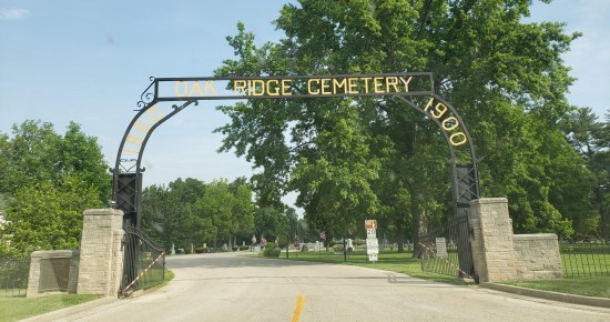 Metal arch reading "Oak Ridge Cemetery 1880 1900" above a road leading into a cemetery. A small brown sign points the way to Lincoln's Tomb.