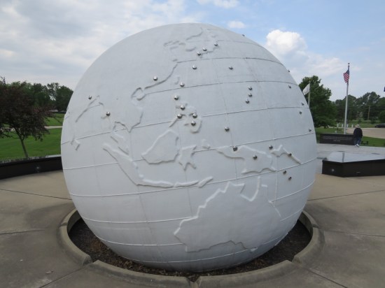 Large all-white globe on an outdoor pedestal. The Pacific Ocean side has metal discs marking locations where Illinoisans died in combat.