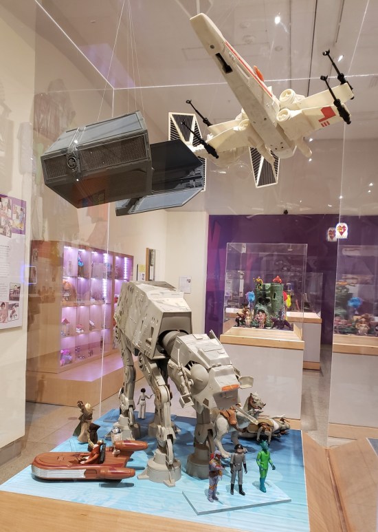Vitrine with an AT-AT, Landspeeder, X-Wing Fighter, TIE Fighter, and a bunch of Star Wars figures.