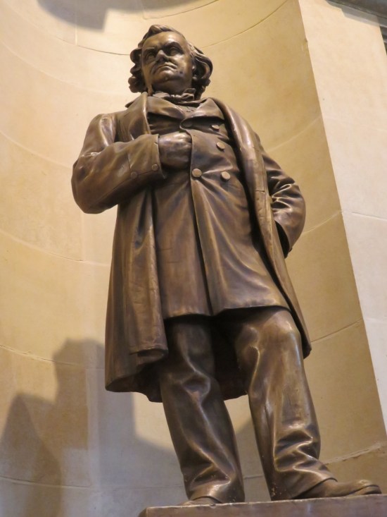 Statue of Stephen Douglas, grumpy and sticking one hand inside his buttoned shirt to scratch his tummy.