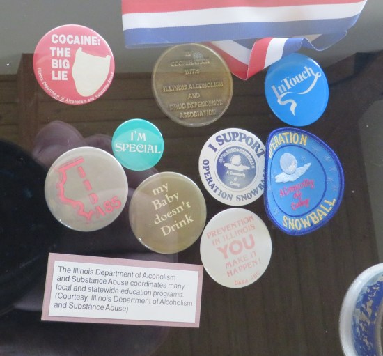 Illinois anti-addiction collectible coins, buttons and patches in a vitrine.