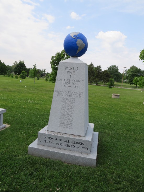 Short white obelisk with a blue globe on top, standing in a cemetery.