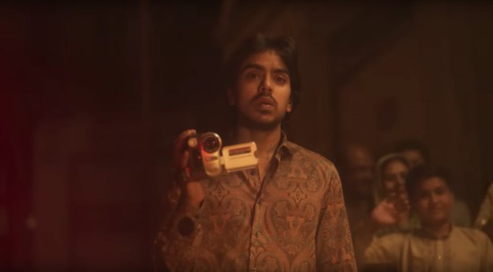 Young filmmaker holding a digital camera, watching forlornly as the woman he loves is driven away offscreen.