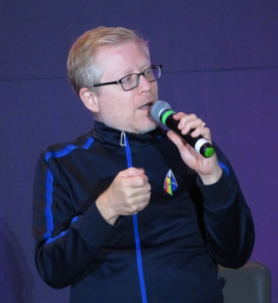 Anthony Rapp talking on stage, turned to one side.