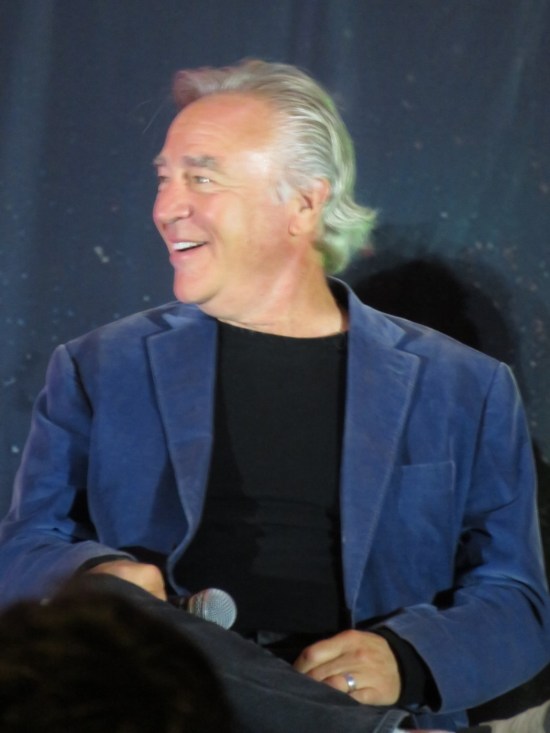 Casey Biggs on stage, sitting and smiling and looking to one side.