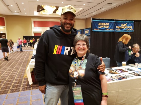 Anne smiling and posing with Cirroc Lofton at his table. He's at least 18 inches taller than she is.