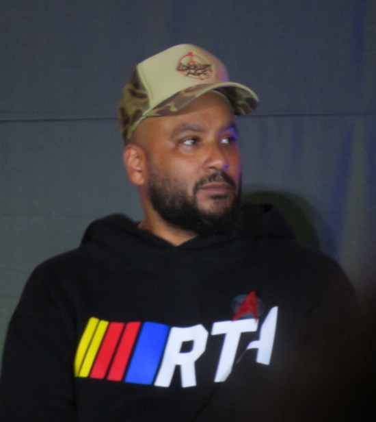 Cirroc Lofton on stage in a black hoodie with an RTA logo and a ball cap reading 
