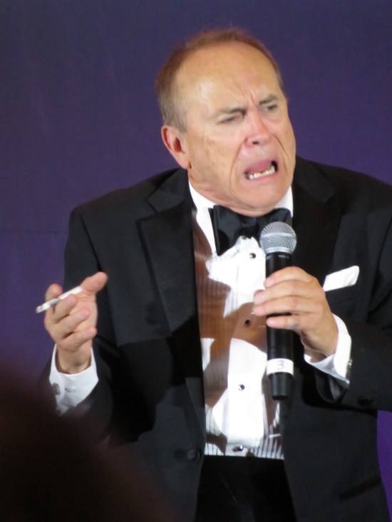 Jeffrey Combs grimacing while wailing into a mic, lit cigarette still in hand.