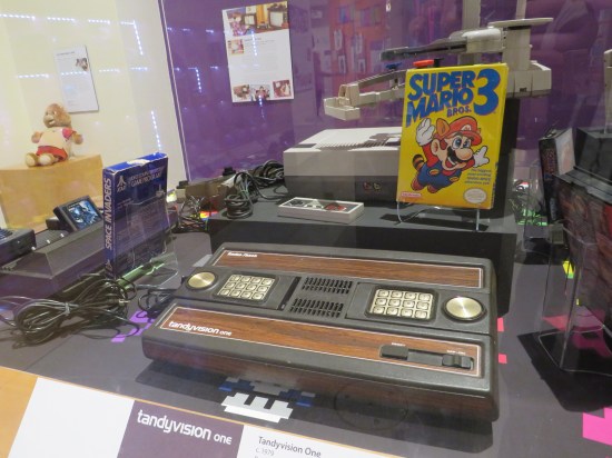 Vitrine housing an Atari 2600, a TandyVision One, and an NES with "Super Mario Bros. 3" standing next to it.