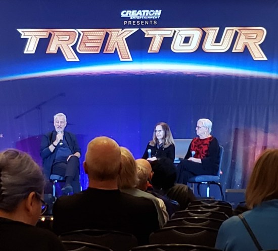 Faraway shot of John de Lancie on the Trek Tour stage with two non-famous women.