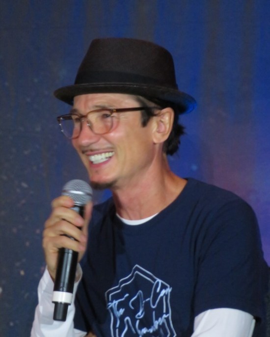 Dominic Keating smiling in hat and glasses.