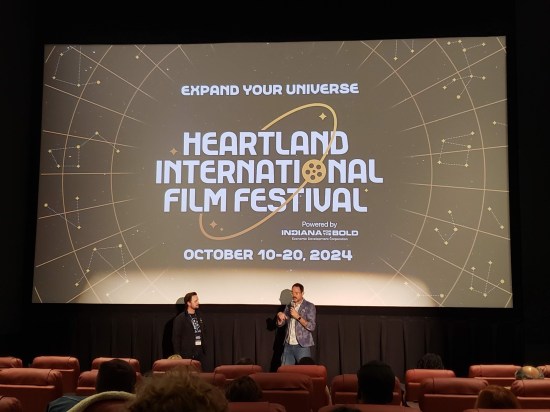 Two men standing at the front of a theater with the Heartland logo on screen.