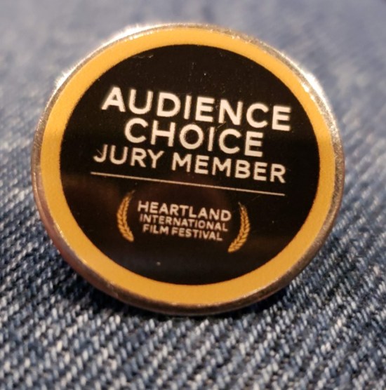 Black pin with yellow border and lettering, "Audience Choice Jury Member, Heartland International Film Festival".