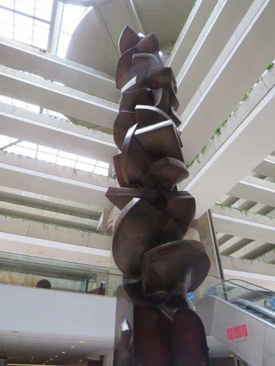 Stories-tall cylindrical statue in an interior hotel courtyard.