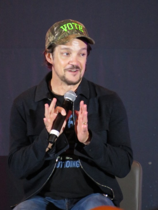 Jonathan Del Arco on stage wearing a camouflage ball cap that says "VOTE".