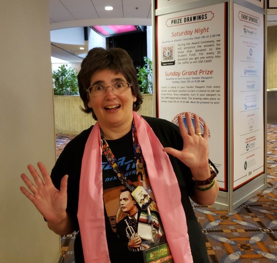 Anne doing jazz hands and wearing a pink sash in front of the neuroscience symposium gateway.